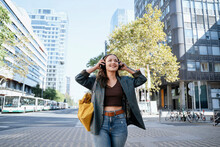 Smiling Woman Listening To Music Through Wireless Headphones In City