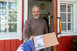 © Westend61 - Smiling man receiving package from delivery person at door