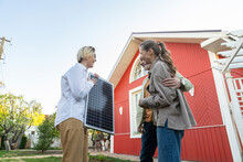 Couple Looking At Solar Panel Held By Agent In Front Of House