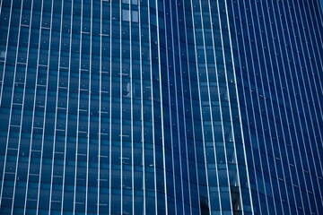 Abstract dark blue facade of an office building. Blue glass facade office building with straight white vertical lines. Modern-looking skyscraper with blue-colored glass windows. Modern city skyline. 