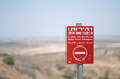 A bright red warning sign outside of the Gaza Strip, near the separation fence around the territory. The sign is trilingual, in Hebrew, Arabic, and English.
