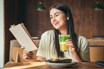 Attractive young woman in a cafe is reading a book with a glass of lemonade.