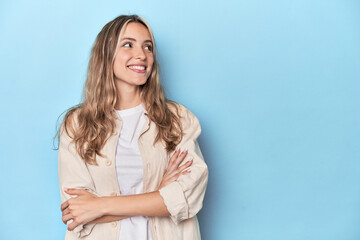 Wall Mural - Blonde young caucasian woman in blue studio smiling confident with crossed arms.