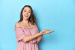 © Asier - Young woman wearing a pink dress on a blue studio backdrop holding a copy space on a palm.