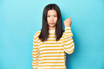 Wall Mural - Asian woman in striped yellow sweater, showing fist to camera, aggressive facial expression.