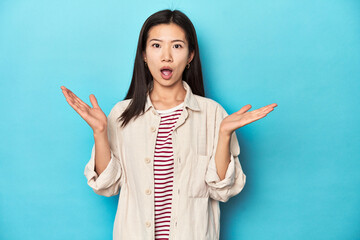 Wall Mural - Asian woman in layered shirt and striped t-shirt, surprised and shocked.