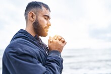 Young Hispanic Man Praying With Closed Eyes At Seaside