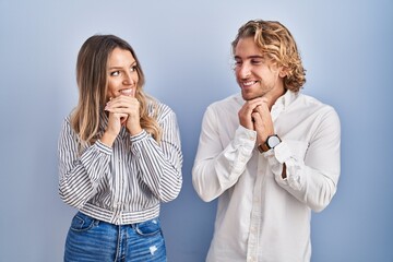 Canvas Print - Young couple standing over blue background laughing nervous and excited with hands on chin looking to the side