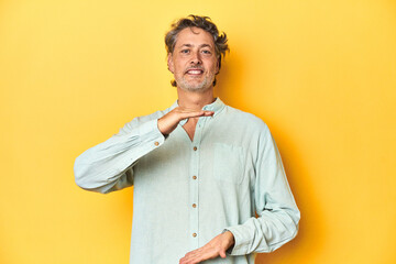 Wall Mural - Middle-aged man posing on a yellow backdrop holding something with both hands, product presentation.