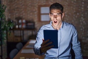 Canvas Print - Handsome hispanic man working at the office at night angry and mad screaming frustrated and furious, shouting with anger. rage and aggressive concept.