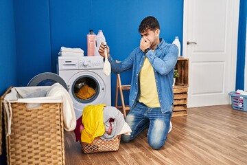 Wall Mural - Young hispanic man smelling dirty sock at laundry room