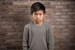 Sadness Asian Boy In A Gray Sweater On Brick Wall Background . Сoncept Coping With Sadness As An Asian Boy, Working With Gray Tones In Fashion, Brick Wall Backdrops In Photography
