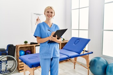 Wall Mural - Young blonde woman pysiotherapist smiling confident writing on document at rehab clinic