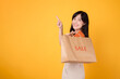 Stylish woman pointing to free copy space while holding bags during a sale isolated on yellow background, enjoying a shopping spree with excitement. Fashion-forward choices.