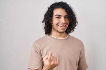 Sticker - Hispanic man with curly hair standing over white background beckoning come here gesture with hand inviting welcoming happy and smiling