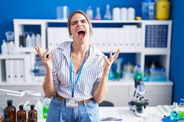 Sticker - Young beautiful woman working at scientist laboratory crazy and mad shouting and yelling with aggressive expression and arms raised. frustration concept.