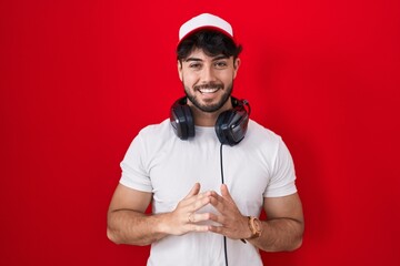 Wall Mural - Hispanic man with beard wearing gamer hat and headphones hands together and fingers crossed smiling relaxed and cheerful. success and optimistic