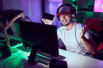 Wall Mural - Hispanic man with beard playing video games with smartphone celebrating achievement with happy smile and winner expression with raised hand