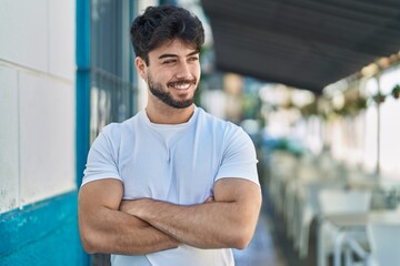 Wall Mural - Young hispanic man smiling confident standing with arms crossed gesture at street