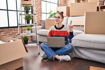 Sticker - Young hispanic girl sitting on the floor at new home with laptop surprised with an idea or question pointing finger with happy face, number one