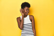 © Asier - Vibrant African woman, white tank-top, yellow studio, trying to listening a gossip.
