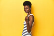 © Asier - Vibrant African woman, white tank-top, yellow studio, pointing with finger at you as if inviting come closer.