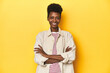 © Asier - African woman, beige shirt, red striped tee, yellow studio, who feels confident, crossing arms with determination.