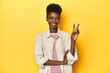© Asier - African woman, beige shirt, red striped tee, yellow studio, showing number two with fingers.