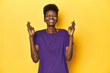 © Asier - African woman in violet tee, yellow studio scene, crossing fingers for having luck