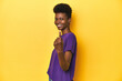 © Asier - African woman in violet tee, yellow studio scene, pointing with finger at you as if inviting come closer.