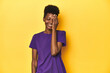 © Asier - African woman in violet tee, yellow studio scene, having fun covering half of face with palm.