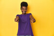 © Asier - African woman in violet tee, yellow studio scene, cheerful smiles pointing to front.