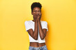 © Asier - African woman, white tee, short hair, yellow studio, laughing about something, covering mouth with hands.