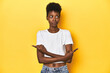 © Asier - African woman, white tee, short hair, yellow studio, points sideways, is trying to choose between two options.