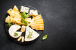 Cheese platter with craft cheese assortment on slate board at black background. Top view with copy space.