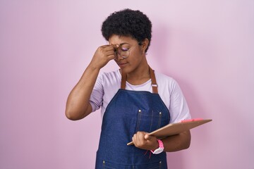 Canvas Print - Young african american woman wearing professional waitress apron holding clipboard tired rubbing nose and eyes feeling fatigue and headache. stress and frustration concept.