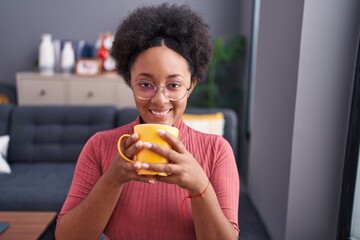 Poster - African american woman drinking coffee sitting on sofa at home