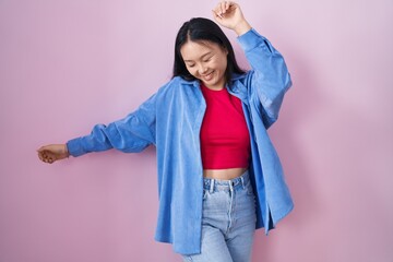 Canvas Print - Young asian woman standing over pink background dancing happy and cheerful, smiling moving casual and confident listening to music