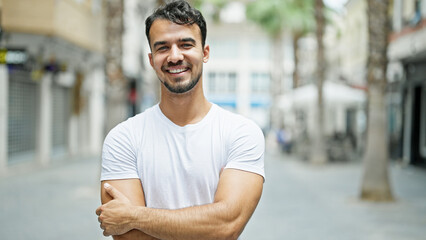 Wall Mural - Young hispanic man smiling confident standing with arms crossed gesture at street