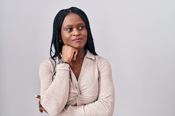 Sticker - African woman with braids standing over white background with hand on chin thinking about question, pensive expression. smiling with thoughtful face. doubt concept.