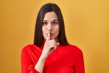 Sticker - Young hispanic woman standing over yellow background asking to be quiet with finger on lips. silence and secret concept.