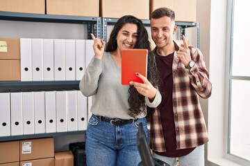 Poster - Young hispanic couple working at small business ecommerce doing video call smiling happy pointing with hand and finger to the side