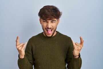 Sticker - Arab man with beard standing over blue background shouting with crazy expression doing rock symbol with hands up. music star. heavy concept.