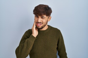 Poster - Arab man with beard standing over blue background touching mouth with hand with painful expression because of toothache or dental illness on teeth. dentist