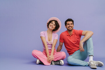 Wall Mural - Young carefree man and woman sitting isolated over purple studio background