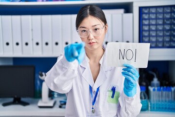 Sticker - Chinese young woman working at scientist laboratory holding no banner pointing with finger to the camera and to you, confident gesture looking serious