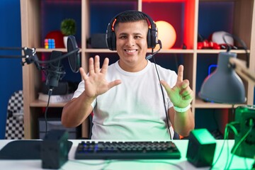 Canvas Print - Young hispanic man playing video games showing and pointing up with fingers number seven while smiling confident and happy.