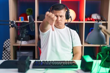 Sticker - Young hispanic man playing video games looking unhappy and angry showing rejection and negative with thumbs down gesture. bad expression.