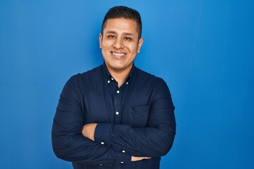 Sticker - Hispanic young man standing over blue background happy face smiling with crossed arms looking at the camera. positive person.