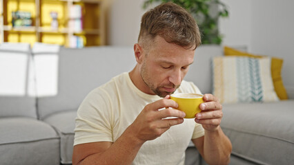 Canvas Print - Young man smelling cup of coffee sitting on floor at home